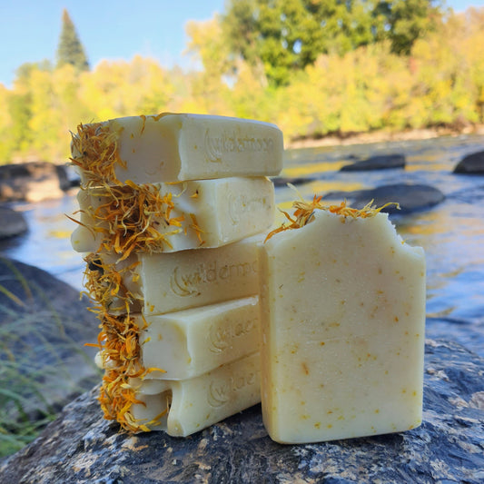 sunburst citrus and calendula artisan handmade soap. rectangular, pale yellow soap with ground calendula specks and dried calendula petals on top with wildermoon logo stamp on side.
