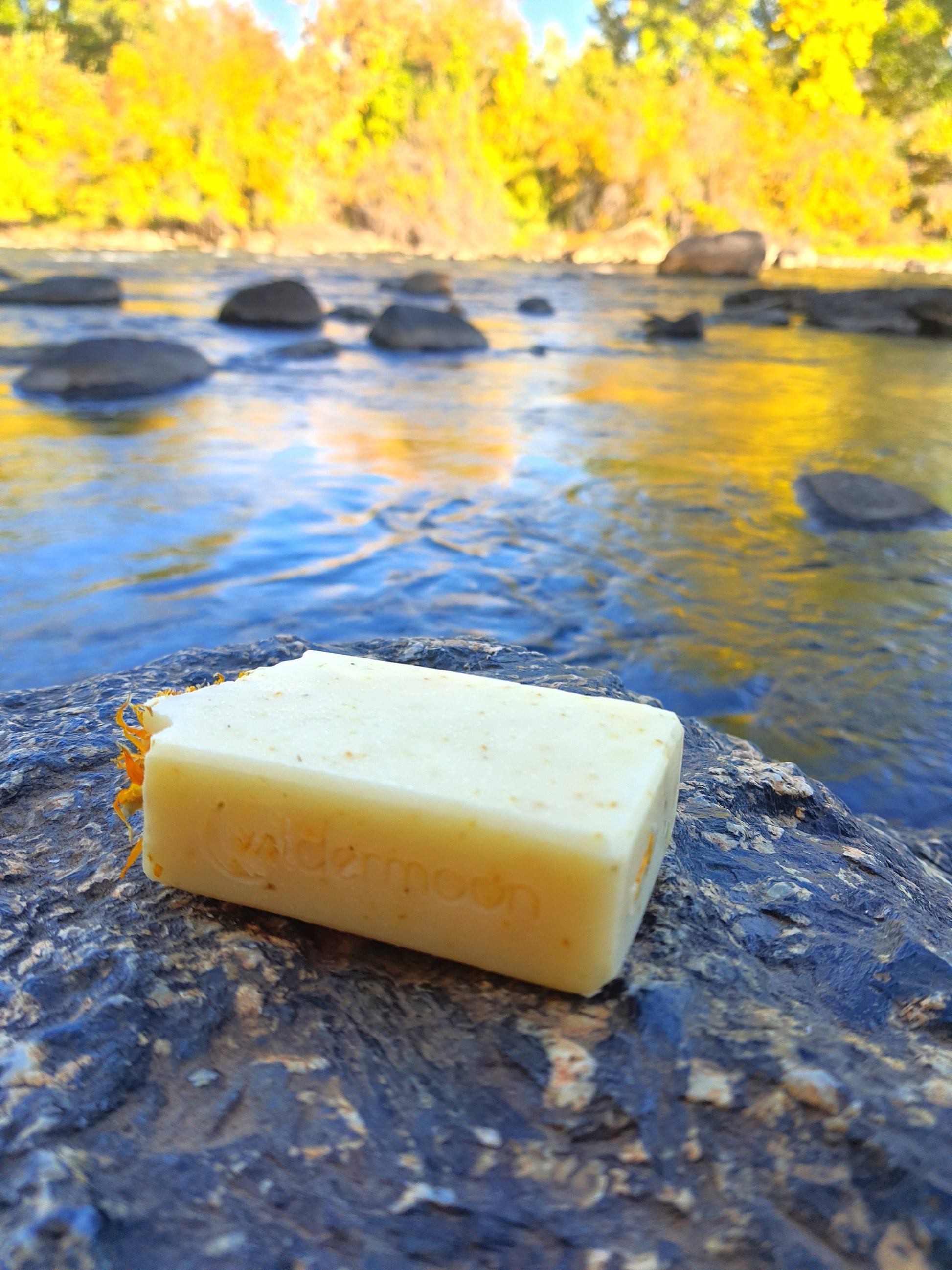 sunburst citrus and calendula artisan handmade soap. rectangular, pale yellow soap with ground calendula specks and dried calendula petals on top with wildermoon logo stamp on side.